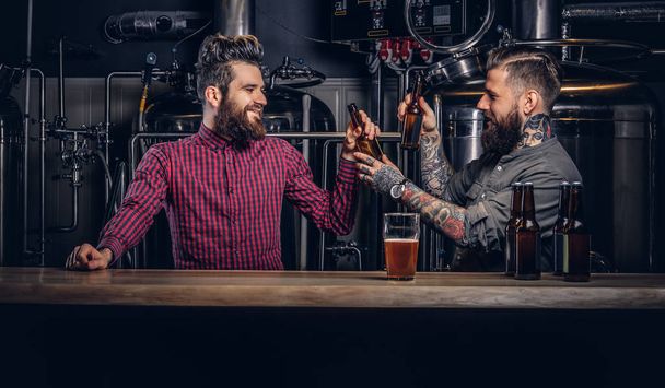 流行に敏感な友人インディーズ醸造所でビールを一緒に飲む 2 つのスタイリッシュなひげを生やした. - 写真・画像