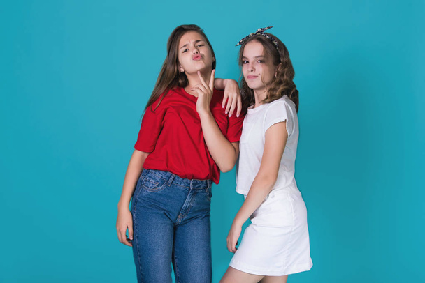 Bild von zwei fröhlichen frechen Mädchen, besten Freundinnen, die Spaß haben und auf blauem Hintergrund lachen. . in stylischer Freizeitkleidung. Raum für Text. süße Teenager-Schulmädchen - Foto, Bild