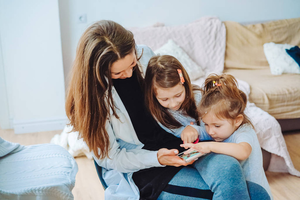 Mom and two daughters are looking at the smartphone - Foto, imagen