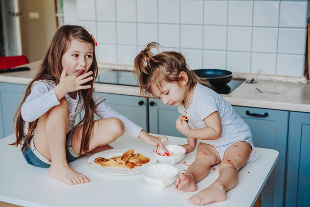 Дві маленькі дівчата на кухні сидять на столі
. - Фото, зображення