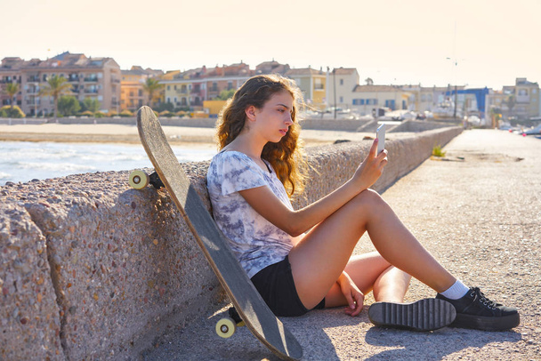 Roller Skate girl with smartphone sitting in a beach dock outdoor - Photo, image