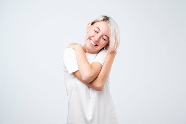 Closeup portret, vertrouwen vrouw in wit t-shirt houden van knuffelen zelf, geïsoleerd witte achtergrond. - Foto, afbeelding