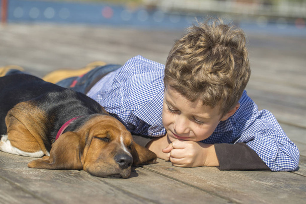  Malý roztomilý chlapec ležící u řeky s jeho štěně. Baví se spolu na krásný a slunečný den. Dospívání, láska pro zvířata - psy, volný čas, cestování, vacatio - Fotografie, Obrázek