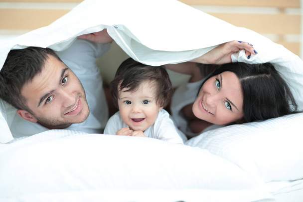 Happy family posing under a duvet while looking at the camera - 写真・画像