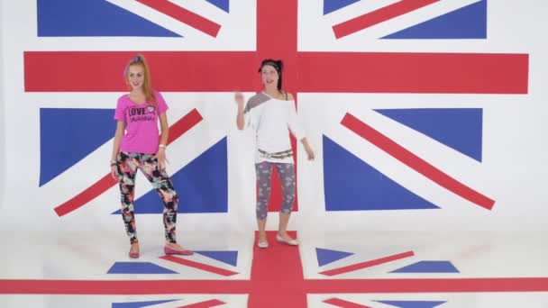 Probe zweier charismatischer Mädchen, die aktiv auf dem Hintergrund der britischen Flagge tanzen - Filmmaterial, Video