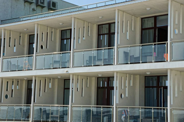 uma fileira de varandas brancas de vidro aberto com móveis na parede do hotel
 - Foto, Imagem