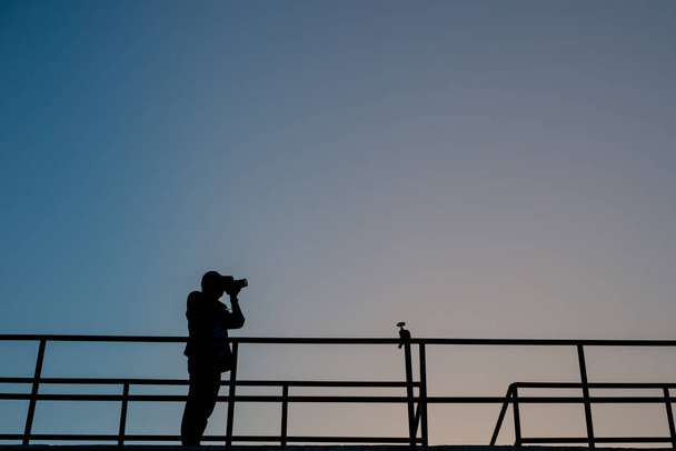La silueta del fotógrafo profesional tomando la foto de la puesta del sol hermosa
 - Foto, Imagen