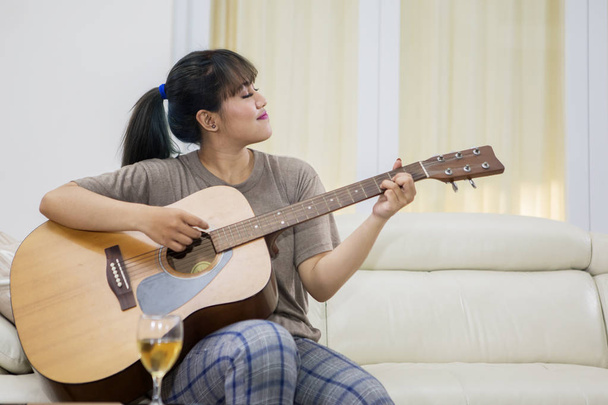Picture of beautiful woman learning to play an acoustic guitar while sitting in the living room - Photo, Image