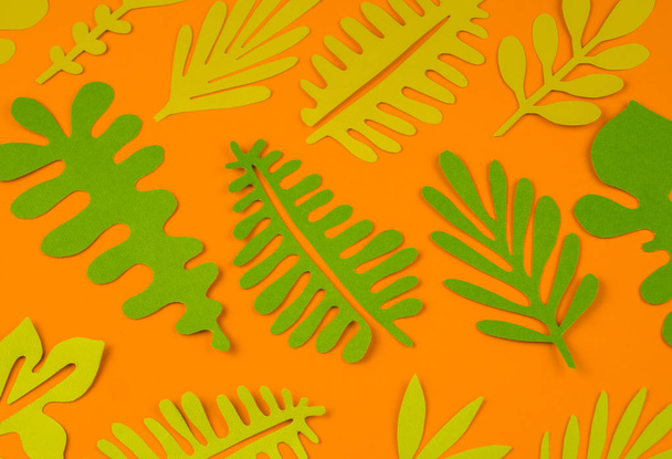 Green leaves made from paper on orange background. Autumn leaf fall. Favorite hobby handicraft. - Фото, изображение