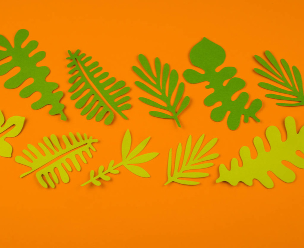 Green leaves made from paper on orange background. Autumn leaf fall. Favorite hobby handicraft. - Фото, изображение