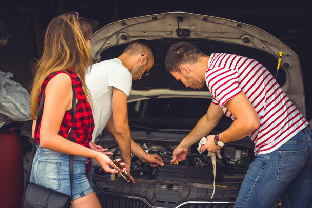 zwei Jungs, die versuchen, ein Auto zu reparieren, während ein Mädchen neben ihnen steht - Foto, Bild