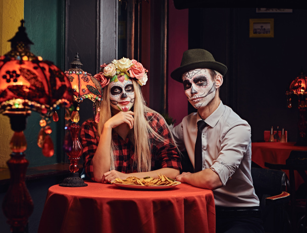 junges attraktives Paar mit untotem Make-up isst Nachos beim Dating in einem mexikanischen Restaurant. - Foto, Bild