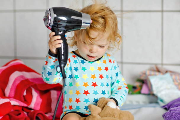 Cute little toddler girl making hairs with hair dryer. Adorable healthy baby child with wet hairs after taking bath. Beautiful girl having fun with toy - Φωτογραφία, εικόνα