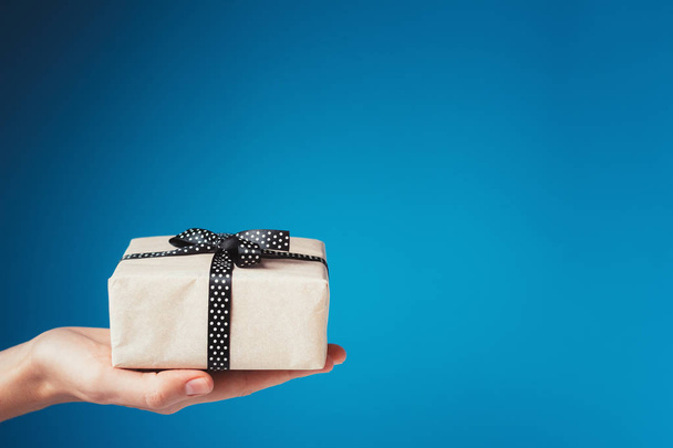 Woman hand holds gift box on palm on blue background with copy space - Fotografie, Obrázek