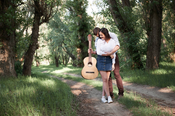 young couple walking in the forest, playing guitar and dancing, summer nature, bright sunlight, shadows and green leaves, romantic feelings - Photo, Image