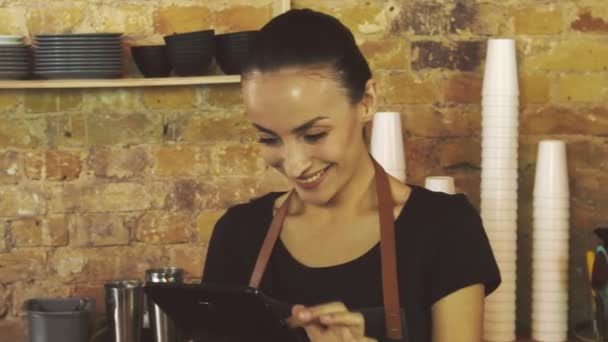 ein attraktives Mädchen (Besitzerin eines Kaffeehauses) arbeitet an einem Tablet. - Filmmaterial, Video