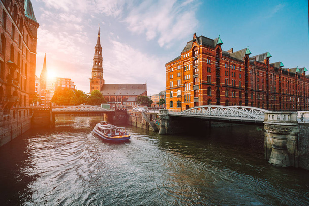 Touristic cruise boat on a channel with bridges in the old warehouse district Speicherstadt in Hamburg in golden hour sunset light, Germany - Foto, Bild