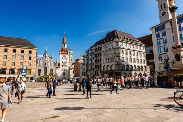 MUNICH, ALEMANHA - SEPT 6, 2018: Turistas e locais passeiam em Marienplatz, a praça da cidade. No fundo o Altes Rathaus (Câmara Municipal Velha) e o Heiliggeistkirche (Igreja do Espírito Santo
)  - Foto, Imagem