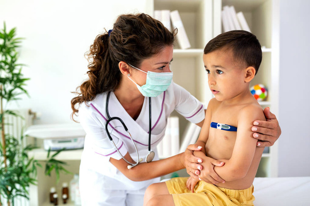 Доктор перевіряє температуру тіла молодого хлопчика, надаючи йому охорону здоров'я, якщо це необхідно
 - Фото, зображення