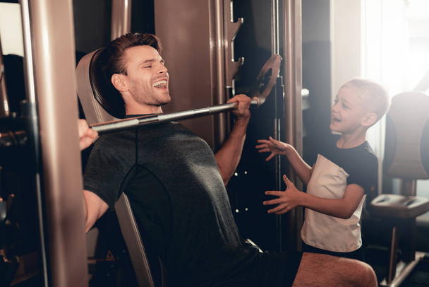 Son Support To Father While Lifting The Barbell. Parenthood Relationship. Sporty Family Concept. Active Lifestyle. Happy Childhood. Holiday Leisure. Working Out Together. Fitness Day. - 写真・画像