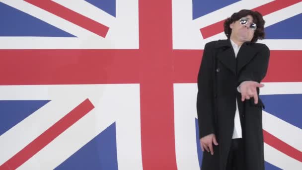 Смешной парень в парике, солнцезащитных очках и пальто поет на камеру в студии с флагом Великобритании
 - Кадры, видео