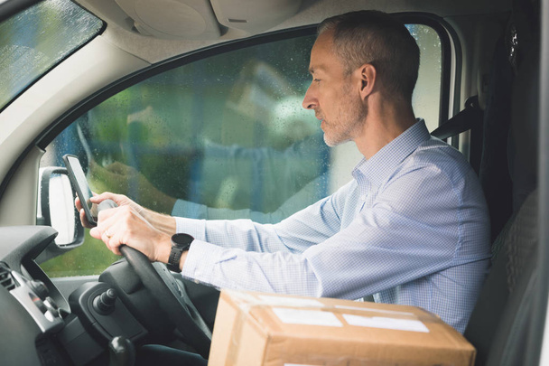 Вид збоку чоловіка доставки з пакетом, що керує фургоном доставки
 - Фото, зображення