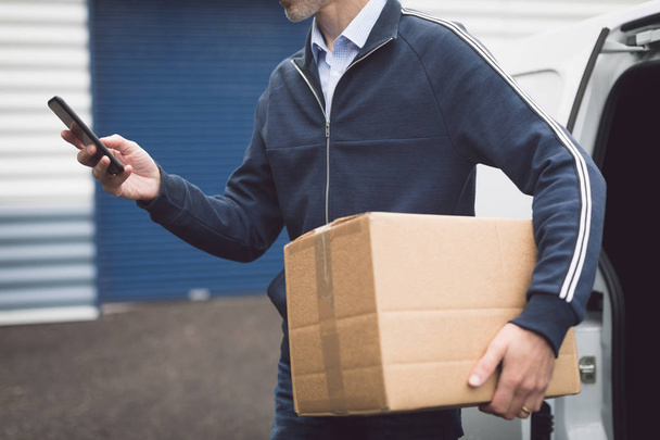 Mid section of delivery man using mobile phone at warehouse - Photo, Image