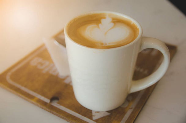 tazza di caffè bianco su piastra di legno su tavolo bianco con schiuma immagine foglia
 - Foto, immagini
