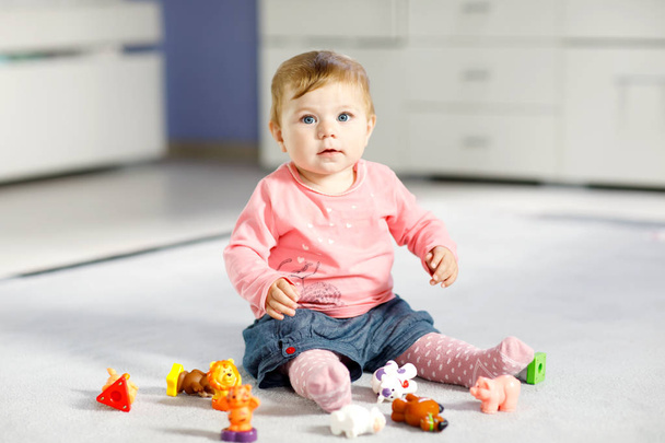Adorable baby girl playing with domestic toy pets like cow, horse, sheep, dog and wild animals like giraffe, elephant and monkey. Happy healthy child having fun with colorful different toys at home - Photo, Image