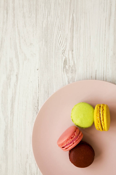 Macarons colorés sur une assiette rose sur une surface en bois blanc, vue de dessus. Gros plan
. - Photo, image