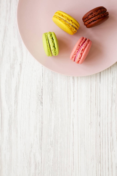 Macarons doux et colorés sur une assiette rose sur fond bois blanc, vue de dessus. Gros plan. Espace de copie
. - Photo, image