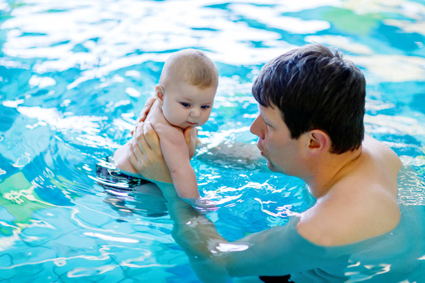 Happy middle-aged father swimming with cute adorable baby in swimming pool. - Photo, Image