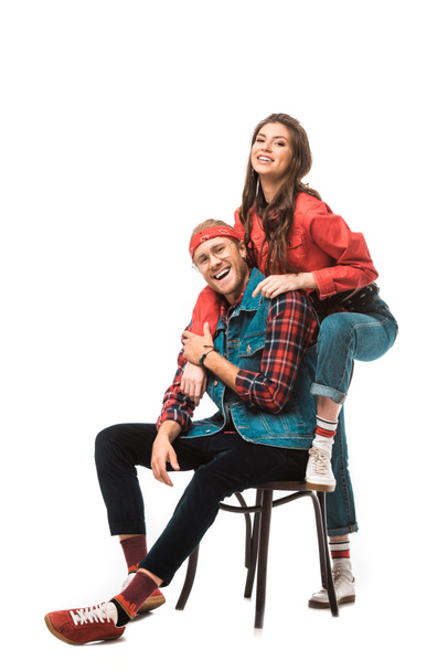 lachen stijlvolle man zit op stoel terwijl zijn hipster meisje permanent achter geïsoleerd op wit - Foto, afbeelding