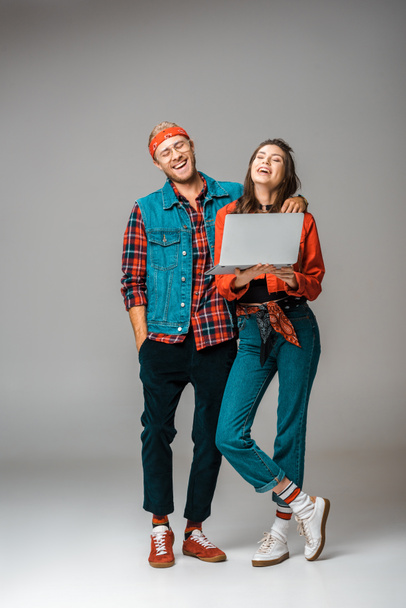 laughing hipster couple standing with laptop on grey - Foto, Bild