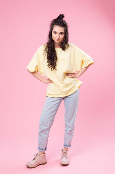 Grimacing beautiful young woman in yellow top is fooling around posing for the camera . Studio portrait on pink background. - Fotoğraf, Görsel