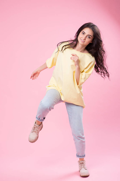 Grimacing beautiful young woman in yellow top is fooling around posing for the camera . Studio portrait on pink background. - Фото, зображення