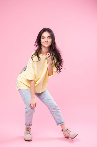 Grimacing beautiful young woman in yellow top is fooling around posing for the camera . Studio portrait on pink background. - Fotó, kép