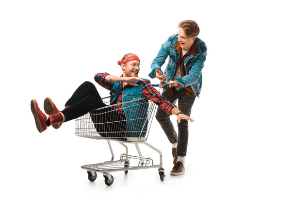 sonriente joven llevando carrito de compras con un amigo varón haciendo gestos con las manos aisladas en blanco
 - Foto, imagen