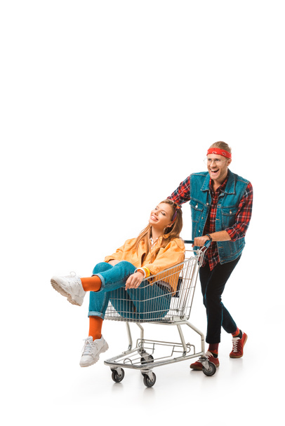 happy young man carrying shopping trolley with girlfriend isolated on white - Foto, Bild