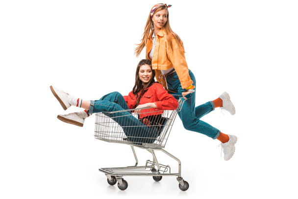 beautiful hipster girl carrying shopping cart with smiling female friend isolated on white - Foto, afbeelding