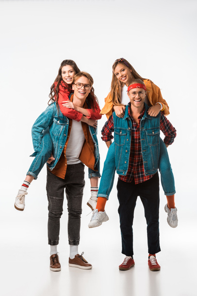 happy stylish hipsters doing piggyback ride to their smiling girlfriends isolated on white - Photo, Image
