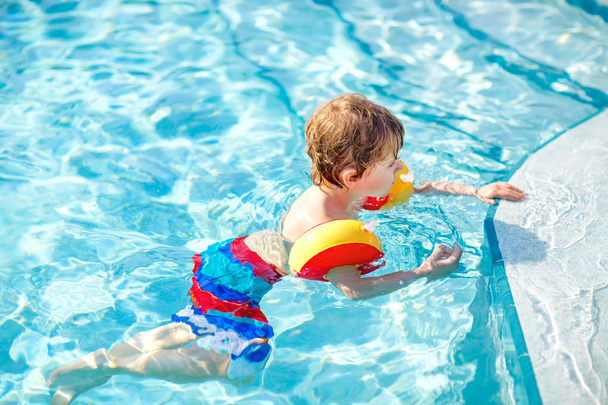 Счастливый маленький мальчик веселится в бассейне. Активный счастливый ребенок учится плавать. с безопасным плаванием или купанием. Семья, отдых, летняя концепция
 - Фото, изображение