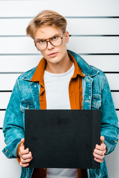 handsome hipster holding empty prison board while standing in front of police line up - Photo, Image