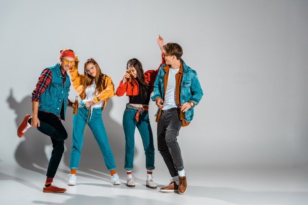 stylish hipsters having fun with beer bottles and dancing together on grey - Photo, Image