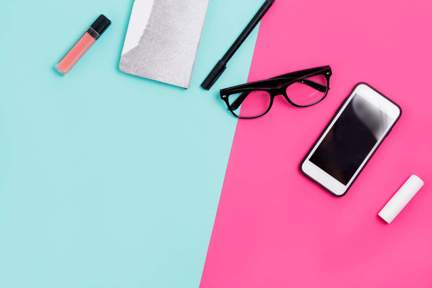 Home office desk with calligraphic pen, glasses, Notepad, smartphone and lipstick on a colorful background with copy space - Photo, image