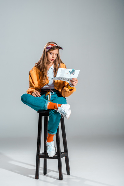 beautiful girl reading travel newspaper while sitting on stool on grey - Fotografie, Obrázek