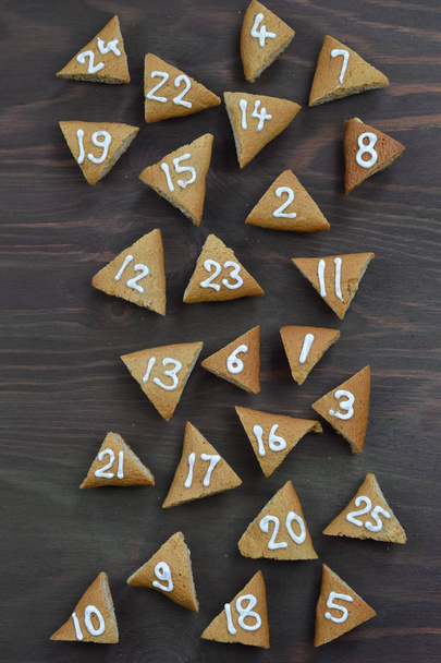 veinticinco galletas de adviento mezcladas numeradas sobre fondo de madera marrón como calendario de adviento
 - Foto, imagen
