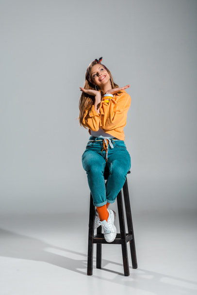 attractive cheerful girl posing on stool on grey - Zdjęcie, obraz