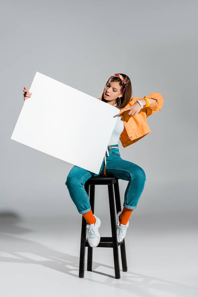 beautiful stylish girl pointing at blank placard on grey - Foto, afbeelding