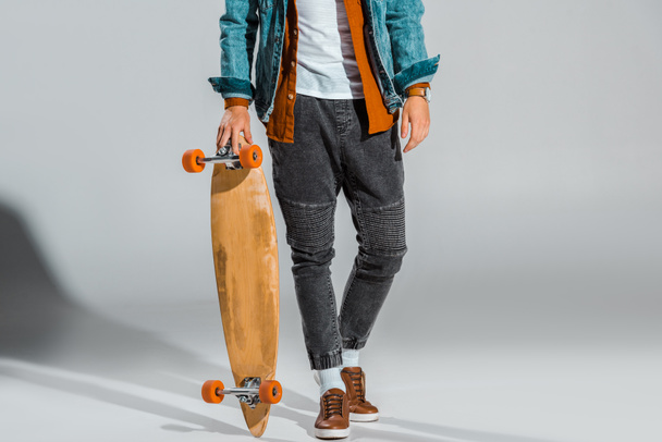 cropped view of young stylish skateboarder posing with longboard on grey - Фото, зображення